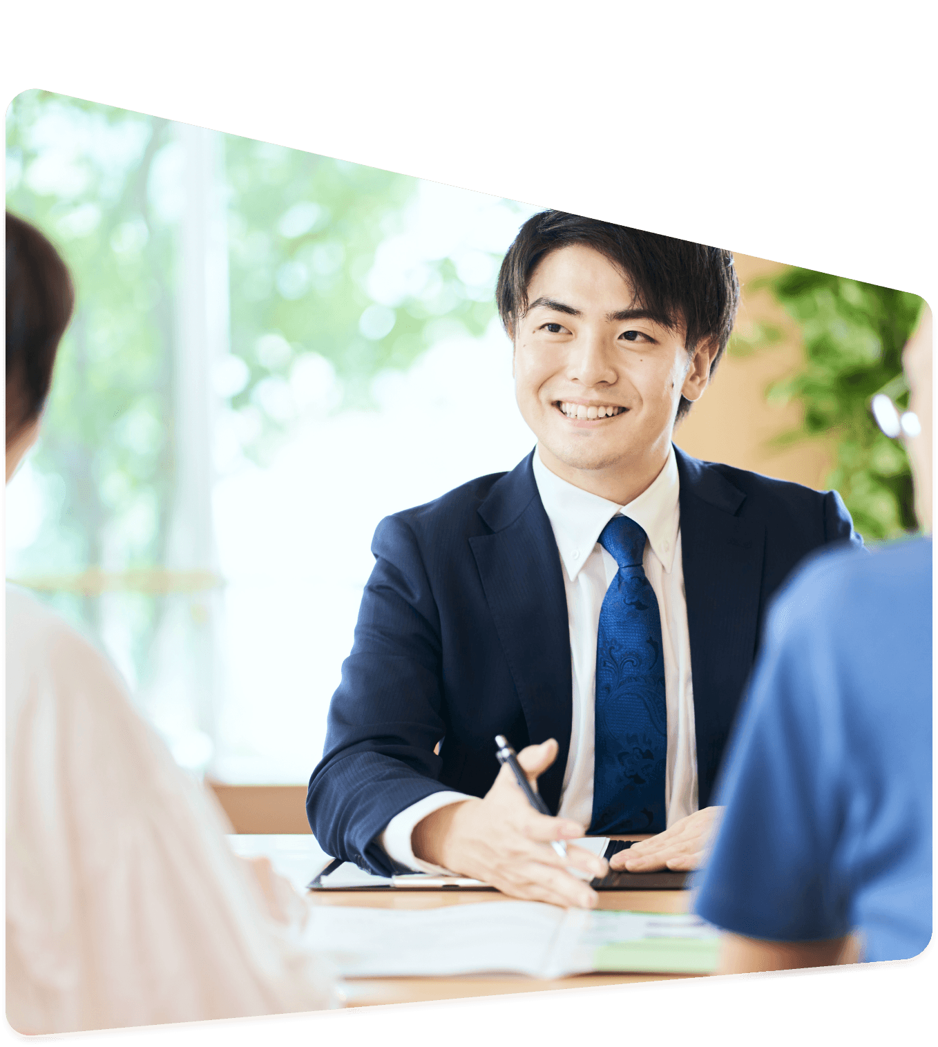 スーツ姿の男性スタッフが笑顔で相談者と対面し、書類を見ながら説明している様子