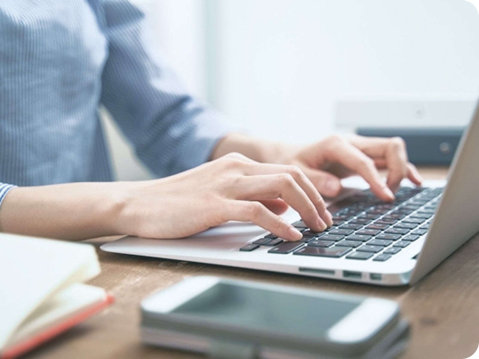 木製デスクでノートパソコンのキーボードに両手を置き、集中してタイピング作業に取り組む営業事務の様子