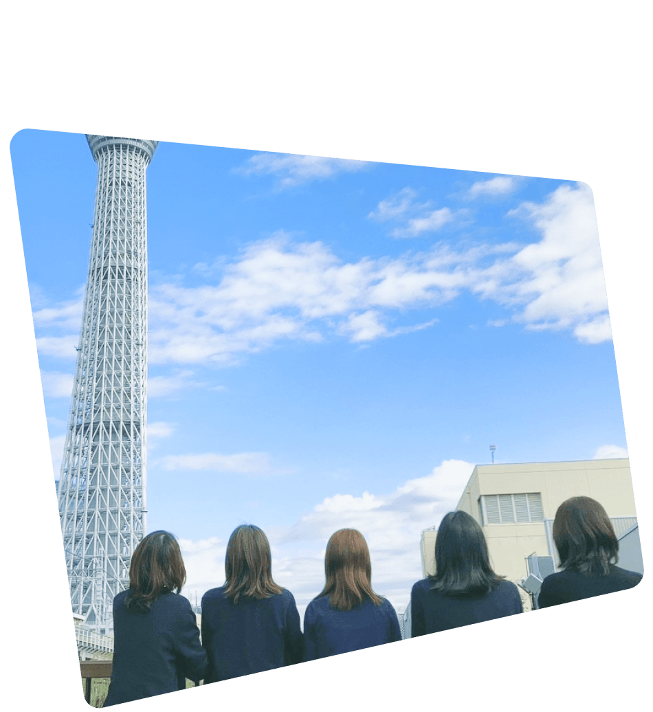青空の下、5人の女性が横一列に並び、背景の東京スカイツリーを見上げている様子