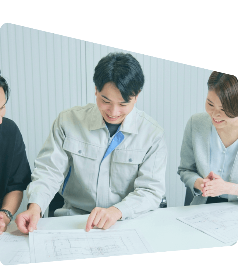 会議室でライトブルーの作業着を着た3人のビジネスパーソンが、資料を見ながら打ち合わせをしている様子