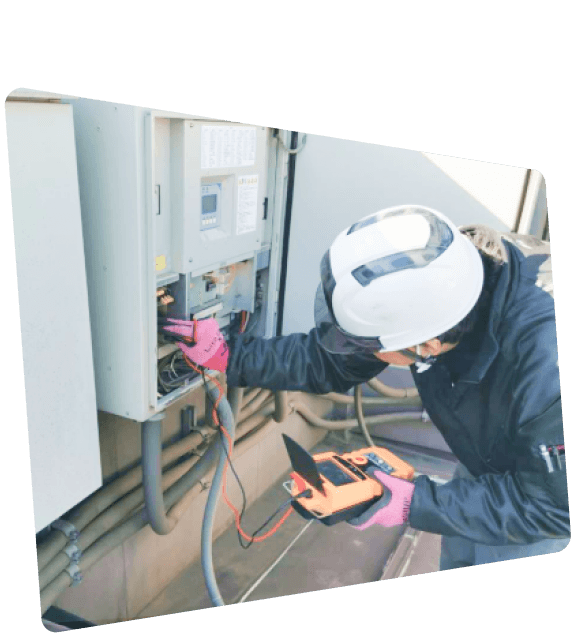 ヘルメットと手袋を着用した技術者が、マルチメーターを使って電気制御盤を点検している様子