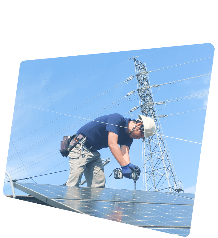 青空の下、ヘルメットと手袋を着用した作業員が太陽光パネルの設置作業を行っている様子