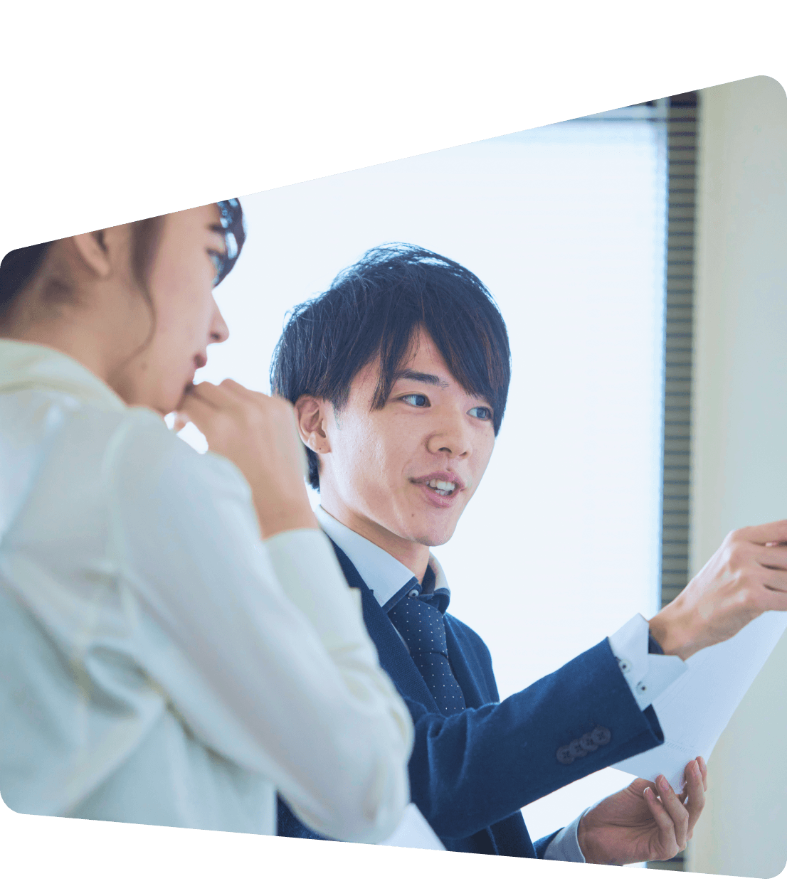 明るいオフィスで、書類を持った男性が説明し、女性が熱心に耳を傾けている対話の様子