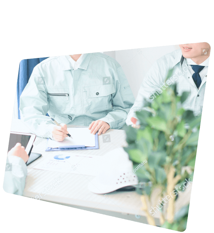 白いテーブルを囲み、設計図のような書類を見ながら笑顔で話し合う3人のビジネスパーソンの様子